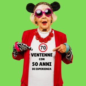 anziana felice con cerchietto con orecchie a topolino che indica la sua maglietta con scritto "ventenne con 50 anni di esperienza"