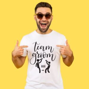 ragazzo felicissimo con occhiali da sole che indica la sua maglietta con scritto "team groom"